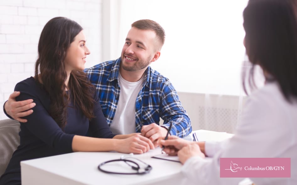 Happy couple sitting across from a doctor in a consultation room, smiling together.