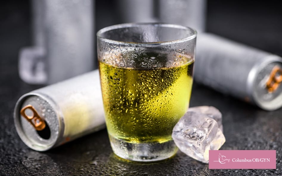 Glass filled with energy drink and ice, surrounded by opened energy drink cans