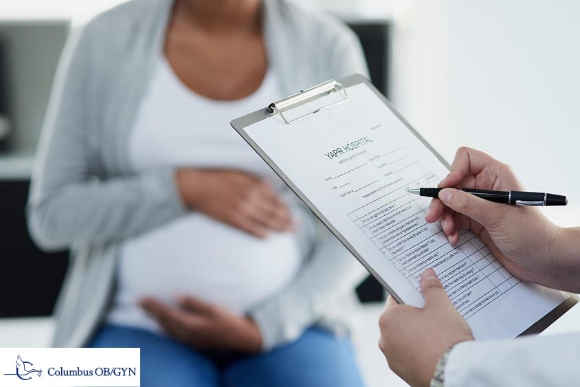 Doctor with results of laboratory test consulting smiling pregnant patient in clinic closeup